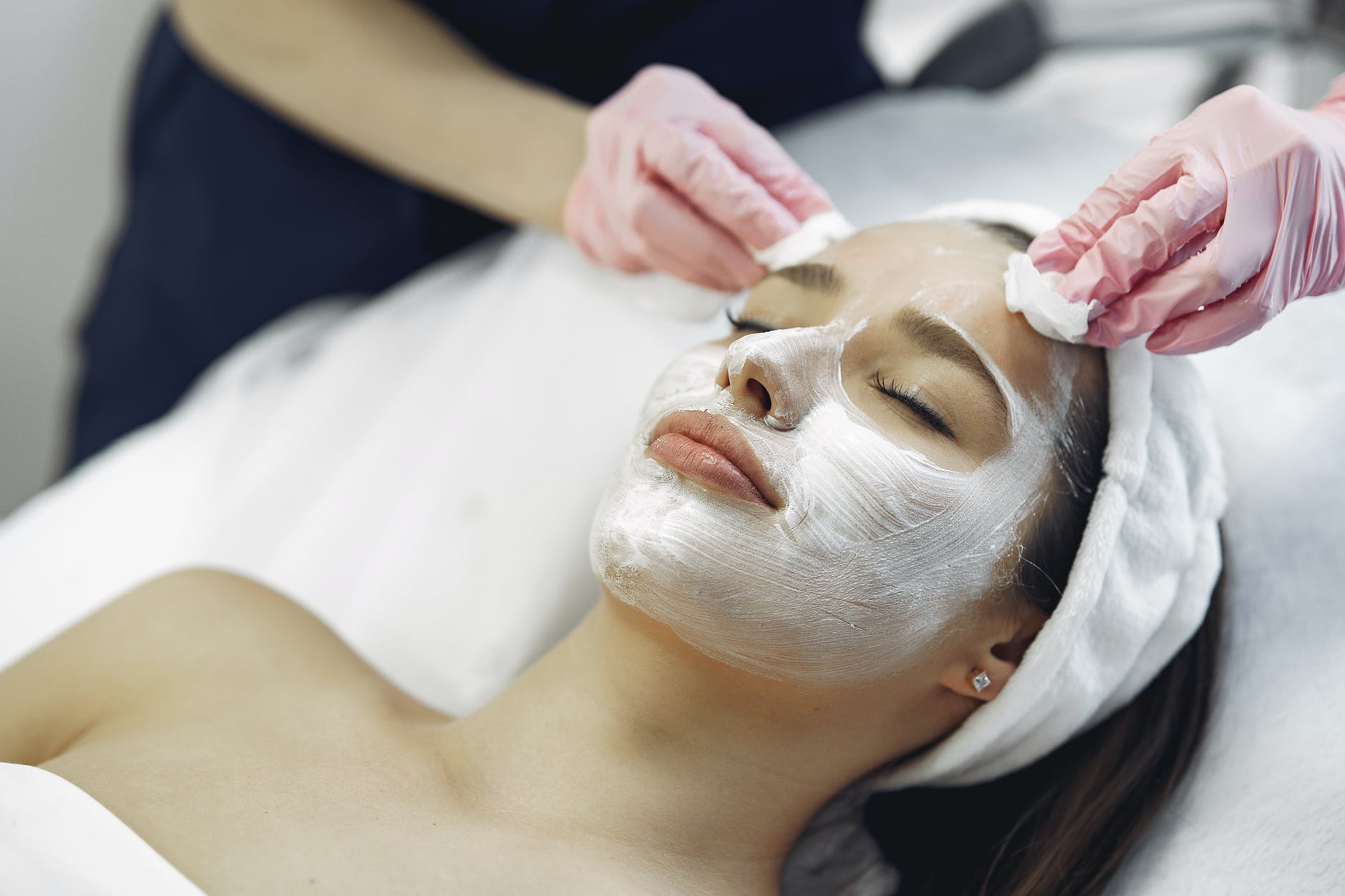 crop woman in medical gloves removing cosmetic mask from face of female client in spa salon